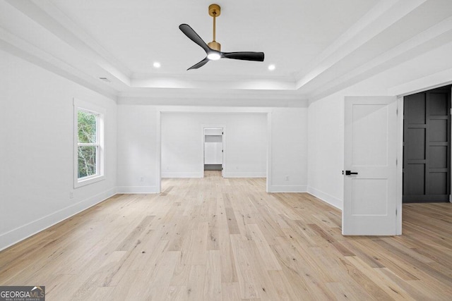 unfurnished living room featuring light hardwood / wood-style floors, ceiling fan, and a raised ceiling