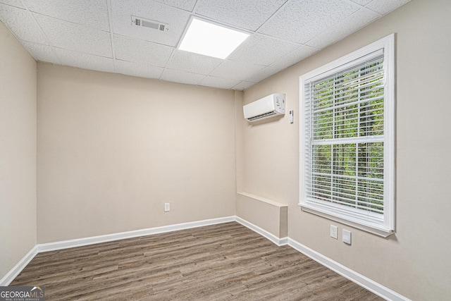 empty room with a paneled ceiling, hardwood / wood-style floors, and a wall mounted air conditioner