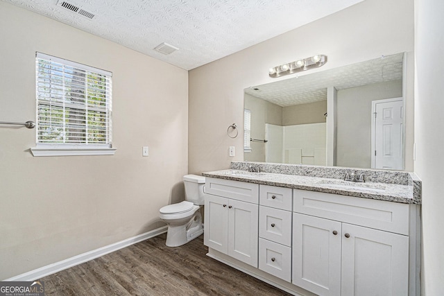 bathroom with a textured ceiling, hardwood / wood-style floors, vanity, toilet, and walk in shower