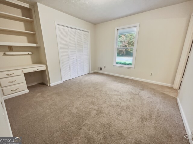 unfurnished bedroom with built in desk and light colored carpet