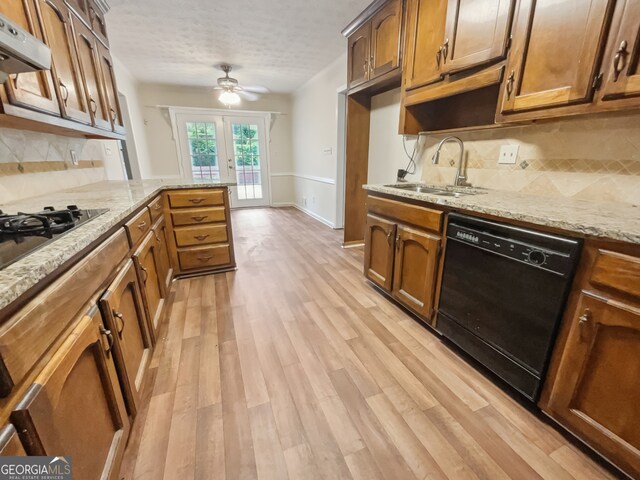 kitchen with backsplash, black appliances, range hood, and light hardwood / wood-style flooring