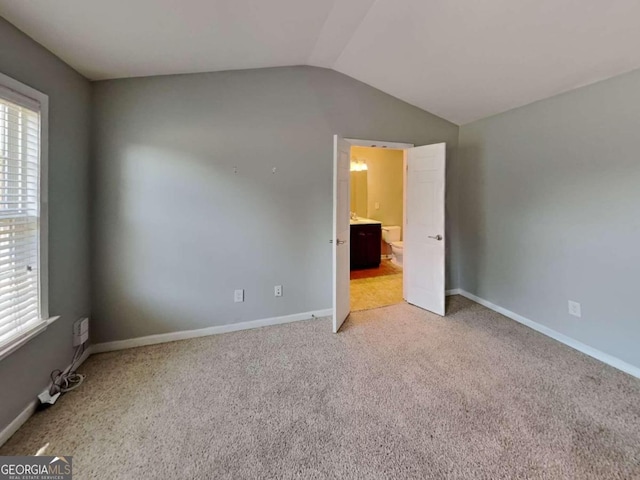 unfurnished bedroom with ensuite bath, light carpet, and vaulted ceiling