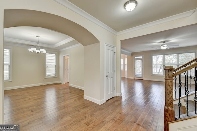 empty room featuring ceiling fan with notable chandelier, light wood-type flooring, and crown molding