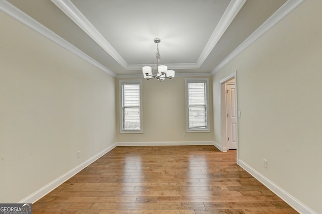 empty room with a chandelier, a raised ceiling, light hardwood / wood-style floors, and crown molding