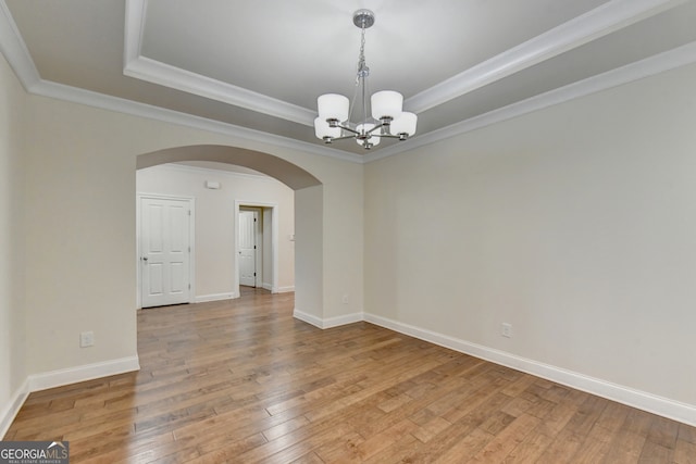 unfurnished room featuring wood-type flooring, a raised ceiling, an inviting chandelier, and ornamental molding