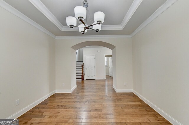 unfurnished dining area featuring a notable chandelier, light hardwood / wood-style flooring, a raised ceiling, and ornamental molding