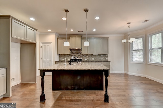 kitchen featuring light stone countertops, hanging light fixtures, hardwood / wood-style floors, a kitchen island with sink, and decorative backsplash