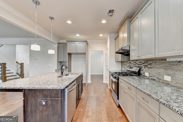 kitchen featuring light hardwood / wood-style floors, appliances with stainless steel finishes, light stone countertops, hanging light fixtures, and an island with sink