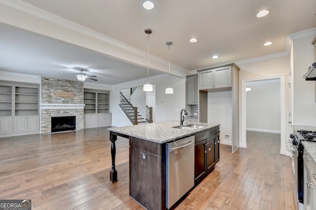 kitchen featuring stainless steel appliances, a center island with sink, sink, light stone counters, and built in shelves