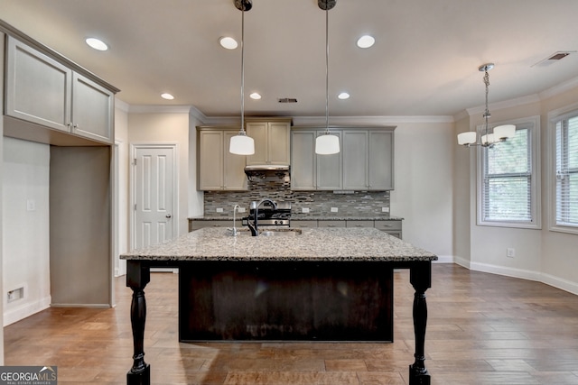 kitchen featuring a center island with sink, decorative light fixtures, light stone countertops, decorative backsplash, and sink