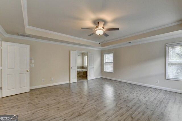 empty room with light hardwood / wood-style floors, ceiling fan, a tray ceiling, and ornamental molding