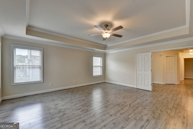 empty room with ceiling fan, light hardwood / wood-style flooring, crown molding, and a tray ceiling