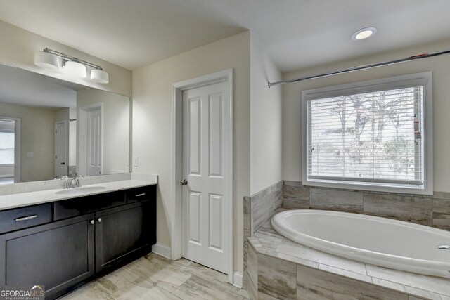 bathroom with a relaxing tiled tub, a wealth of natural light, and vanity