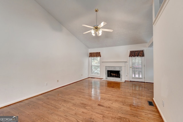 unfurnished living room with ceiling fan, a high end fireplace, light wood-type flooring, and high vaulted ceiling