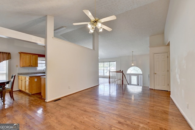 unfurnished living room featuring high vaulted ceiling, a textured ceiling, ceiling fan, and light hardwood / wood-style flooring