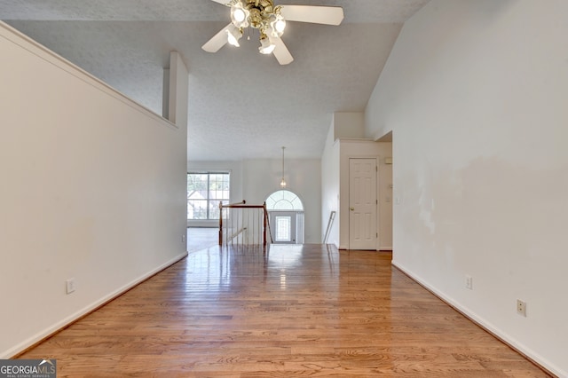 unfurnished living room featuring high vaulted ceiling, light hardwood / wood-style floors, a textured ceiling, and ceiling fan