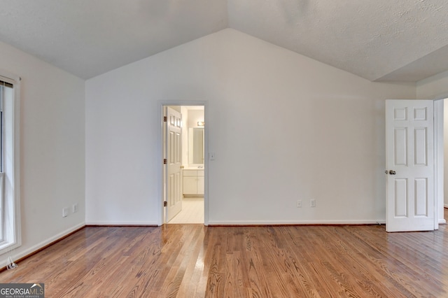 unfurnished room with a textured ceiling, hardwood / wood-style flooring, and vaulted ceiling