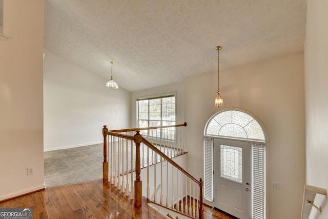 foyer with hardwood / wood-style flooring, a chandelier, a textured ceiling, and vaulted ceiling