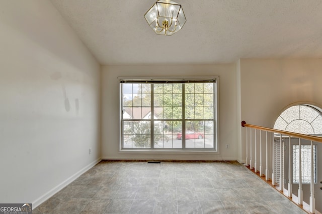 spare room featuring a chandelier, a healthy amount of sunlight, a textured ceiling, and vaulted ceiling