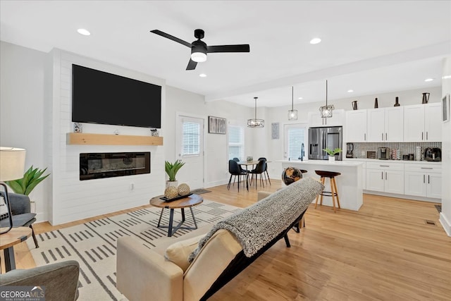 living room featuring light wood-type flooring, ceiling fan with notable chandelier, and a fireplace