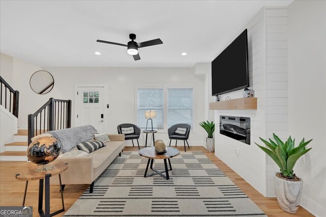 living room with light hardwood / wood-style floors, ceiling fan, and a large fireplace