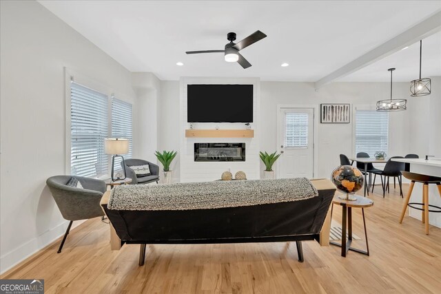 living room with beamed ceiling, light hardwood / wood-style flooring, and ceiling fan with notable chandelier