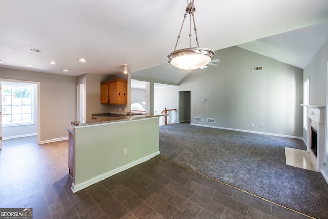 kitchen with dark colored carpet, lofted ceiling, kitchen peninsula, pendant lighting, and dark stone countertops