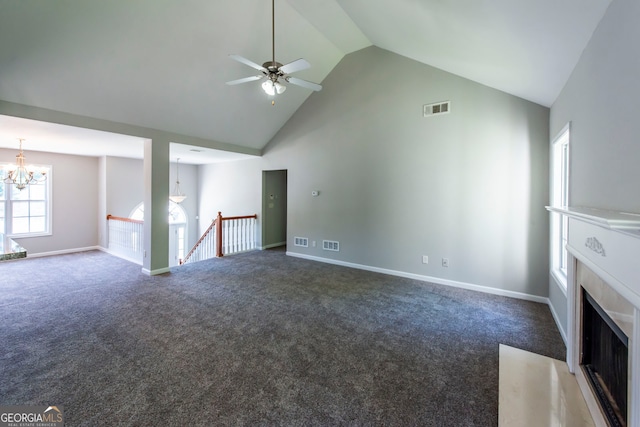 unfurnished living room with high vaulted ceiling, ceiling fan with notable chandelier, and dark colored carpet