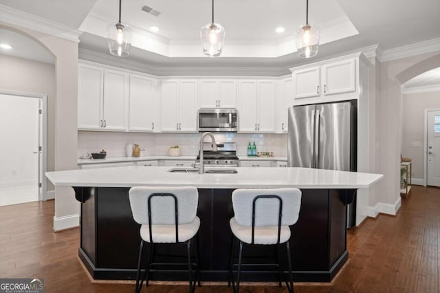 kitchen with dark wood-type flooring, crown molding, an island with sink, white cabinets, and appliances with stainless steel finishes