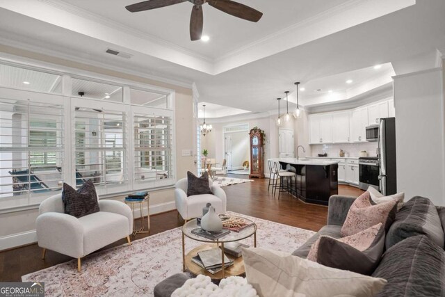 living room featuring ornamental molding, ceiling fan with notable chandelier, a raised ceiling, sink, and dark hardwood / wood-style floors