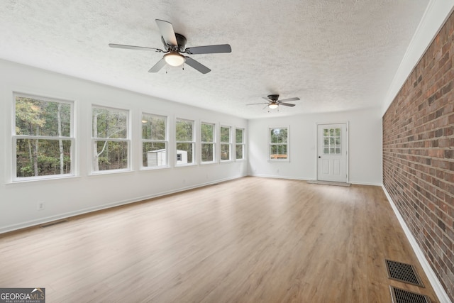 unfurnished living room featuring light wood-type flooring, brick wall, and a textured ceiling