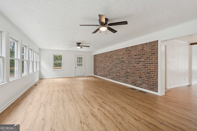 unfurnished living room featuring ceiling fan, a textured ceiling, brick wall, and light wood-type flooring