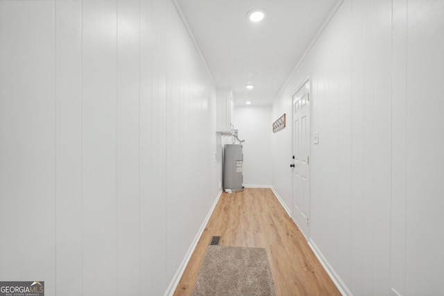 hall featuring water heater, wood walls, ornamental molding, and light hardwood / wood-style flooring