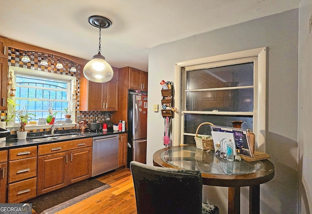 kitchen featuring sink, appliances with stainless steel finishes, hanging light fixtures, light hardwood / wood-style flooring, and decorative backsplash