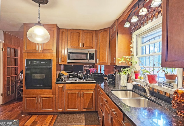 kitchen with stainless steel appliances, sink, dark stone counters, hanging light fixtures, and dark hardwood / wood-style flooring