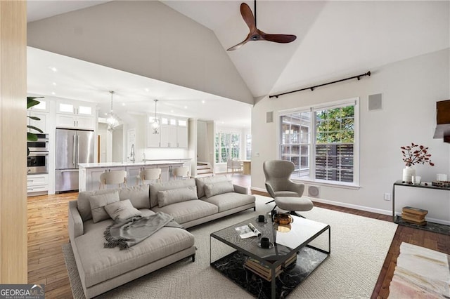 living room featuring hardwood / wood-style floors, ceiling fan with notable chandelier, sink, and high vaulted ceiling