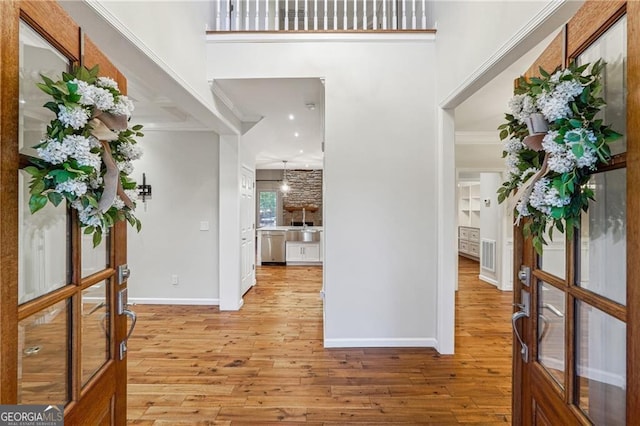 entryway featuring a towering ceiling, french doors, ornamental molding, and light hardwood / wood-style flooring