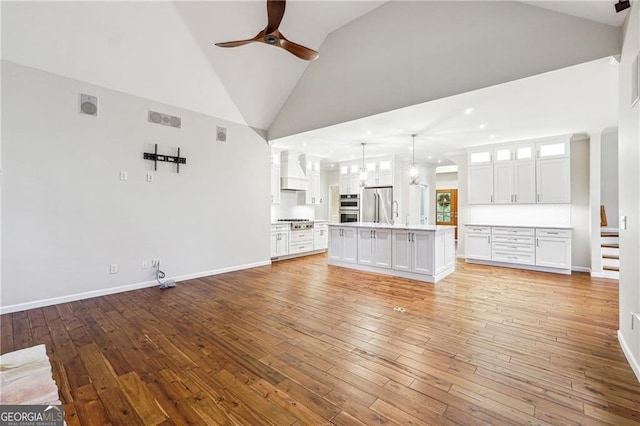 unfurnished living room featuring light hardwood / wood-style floors, ceiling fan with notable chandelier, and high vaulted ceiling