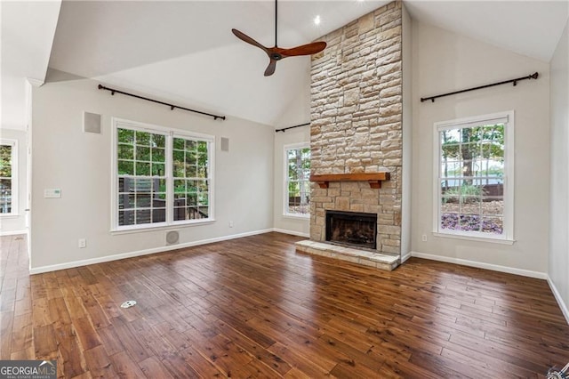 unfurnished living room with high vaulted ceiling, a fireplace, a healthy amount of sunlight, and dark hardwood / wood-style flooring