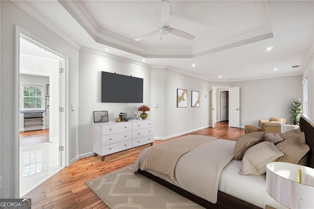 bedroom with ornamental molding, a tray ceiling, ceiling fan, and light hardwood / wood-style flooring