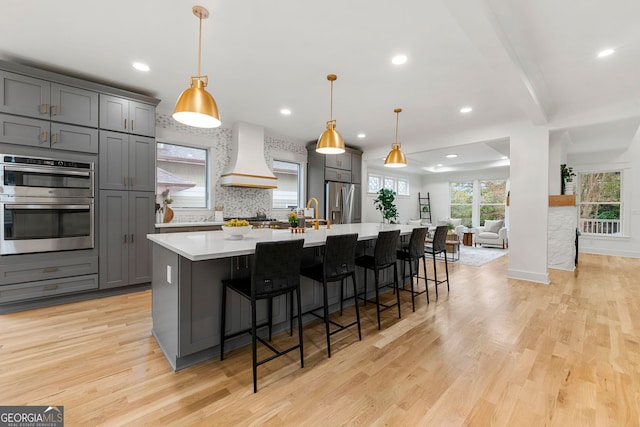 kitchen with gray cabinetry, light hardwood / wood-style flooring, decorative backsplash, and stainless steel counters