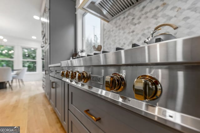 kitchen with appliances with stainless steel finishes, light wood-type flooring, an island with sink, gray cabinets, and pendant lighting