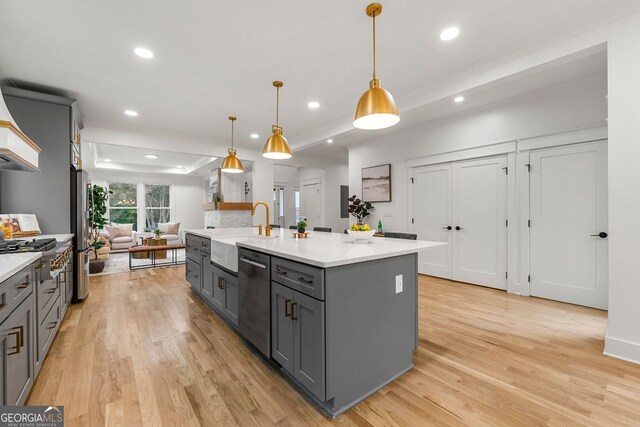 kitchen with light hardwood / wood-style floors, sink, gray cabinetry, a large island with sink, and decorative light fixtures