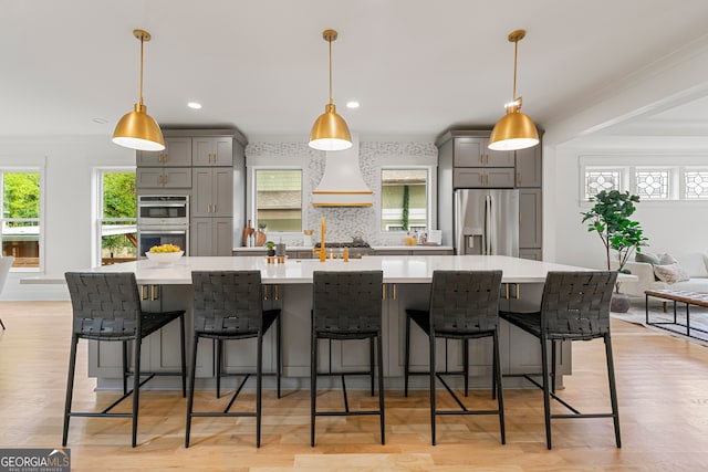 kitchen featuring gray cabinetry, stainless steel appliances, decorative light fixtures, custom range hood, and a spacious island