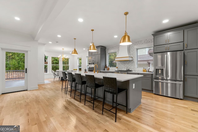 kitchen with stainless steel appliances, decorative backsplash, gray cabinetry, custom range hood, and light hardwood / wood-style flooring