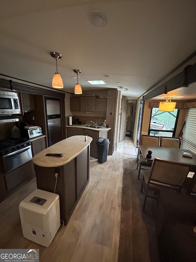 kitchen featuring stainless steel appliances, light hardwood / wood-style floors, sink, a kitchen island, and pendant lighting