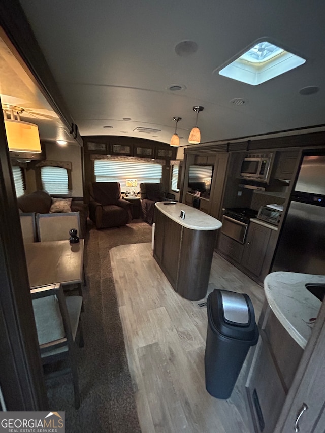 kitchen with a center island, stainless steel microwave, a skylight, light hardwood / wood-style flooring, and decorative light fixtures