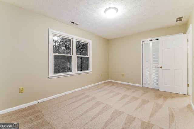 unfurnished bedroom featuring light colored carpet, a textured ceiling, and a closet