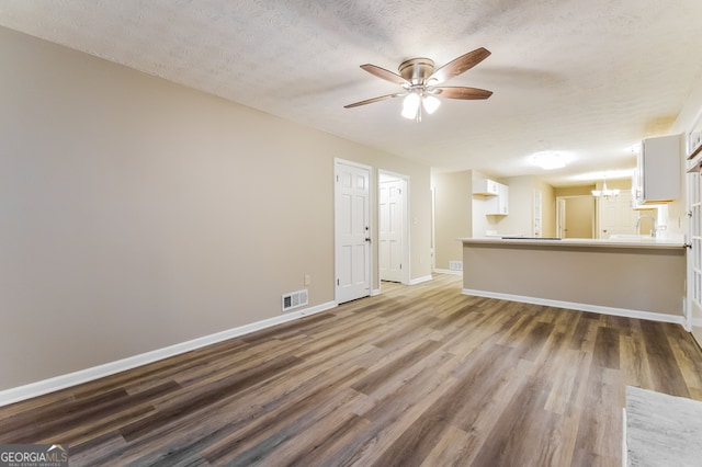 unfurnished living room with ceiling fan with notable chandelier, a textured ceiling, sink, and dark hardwood / wood-style flooring