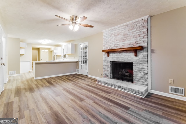 unfurnished living room featuring a brick fireplace, light hardwood / wood-style floors, ceiling fan, and a textured ceiling